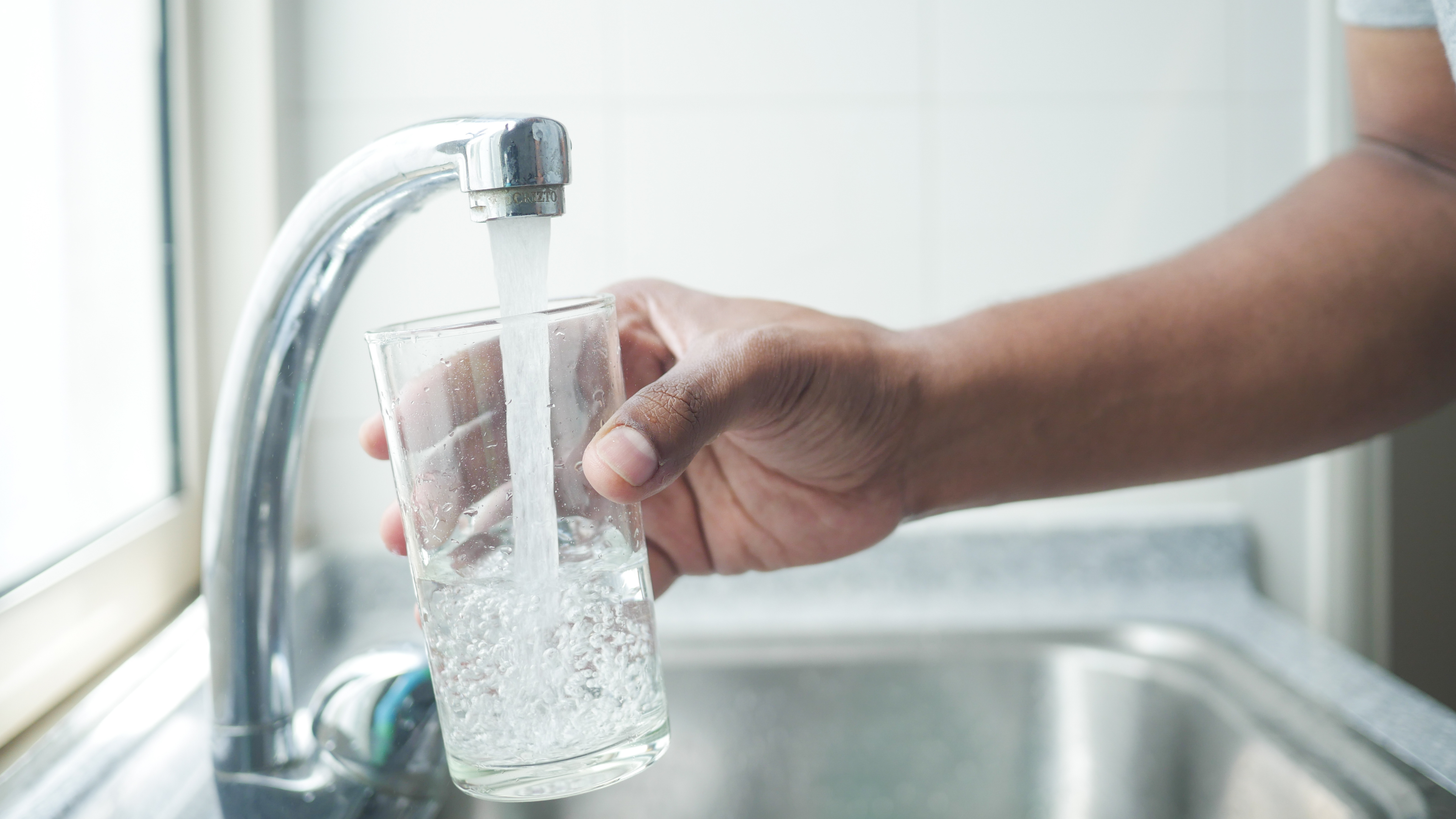 person filling glass of water at kitchen sink